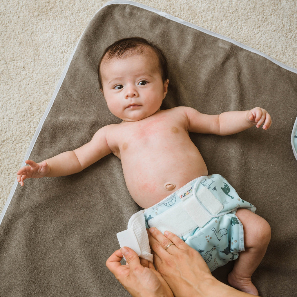Μωρό ξαπλωμένο σε γκρι σελτεδάκι φοράει υφασμάτινη πάνα Popolini και βρακάκι πάνας Popowrap.