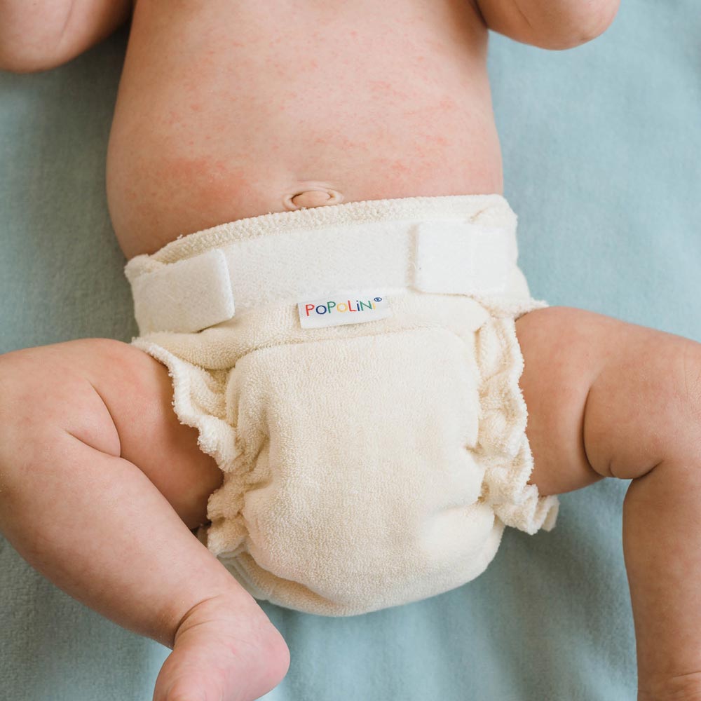 Νεογέννητο μωρό ξαπλωμένο σε σελτεδάκι γαλάζιο, φοράει υφασμάτινη πάνα για νεογέννητο Minifit Popolini σε φυσικό χρώμα. 