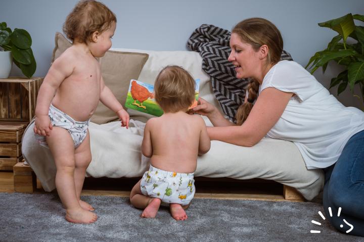 Δυο παιδάκια με την μαμά του διαβάζουν βιβλίο και φοράνε Υφασμάτινες Πάνες Μωρού Σετ MaxiSnap 'Soft' Popolini με καλλυμμα popowrap λευκό με ζωάκια.
