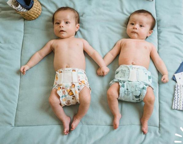 Δυο νεογέννητα μωρά ξαπλωμένα σε σελτεδάκι γαλάζιο, φοράνε υφασμάτινη πάνα για νεογέννητο Minifit Popolini με βρακάκια πάνας σε σχέδιο ζώα της ζούγκλας και γαλάζιο με δεινόσαυρου.