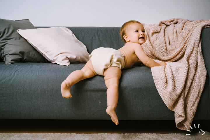 Χαμογελαστό μωρό κατεβαίνει από γκρι καναπέ και φοράει Κάλυμμα Πάνας Wool Wrap
