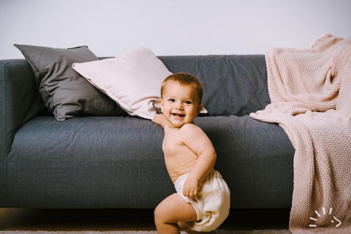 Χαμογελαστό μωρό δίπλα απο γκρι καναπέ και φοράει Κάλυμμα Πάνας Wool Wrap