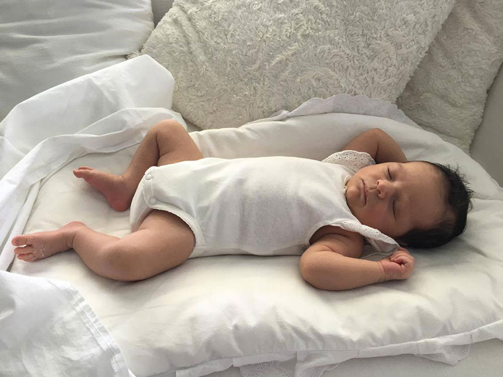 Νεογέννητο μωρό με λευκό φορμάκι ξαπλωμένο σε στρωματάκι αγκαλιάς με λευκή θήκη