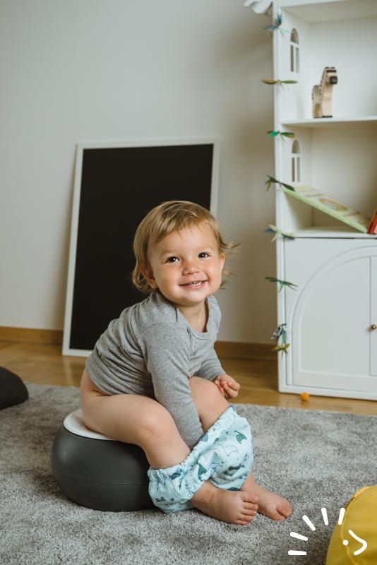 Χαμογελαστό μωρό κάθεται σε γιογιό και φοράει γκρι μπλούζα και Βρακάκι Εκμάθησης Μωρού Popolini