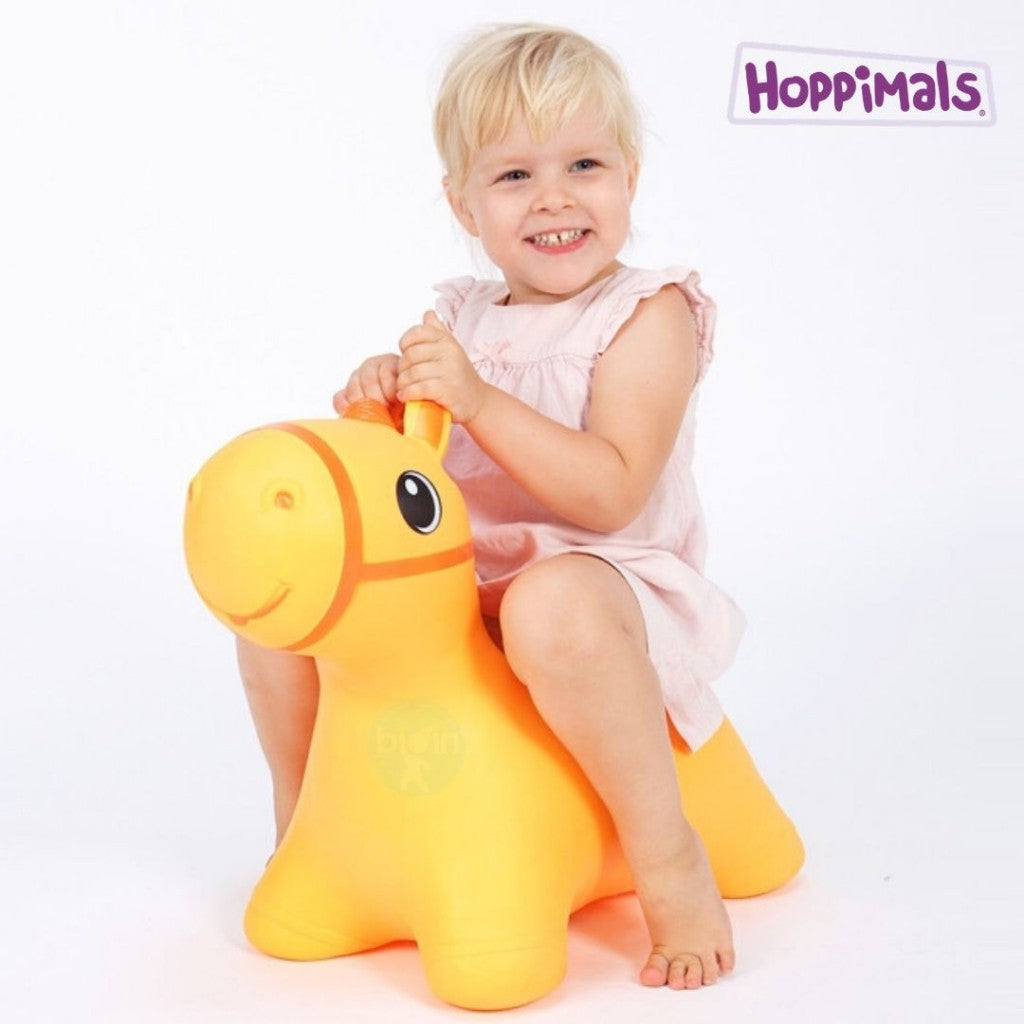 Ξανθό κοριτσάκι που φοράει φόρεμα είναι πάνω σε φουσκωτό χοπ χοπ άλογο σε χρώμα πορτοκαλί.