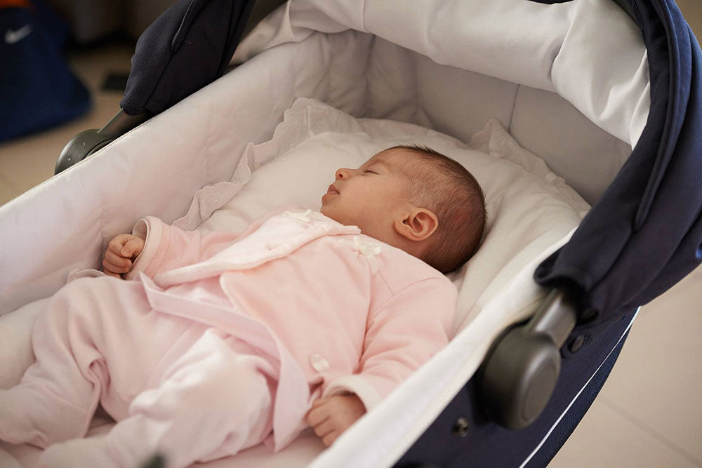 Νεογέννητο μωρό με ροζ φορμάκι ξαπλωμένο σε μπλέ καρότσι με στρωματάκι αγκαλιάς με λευκή θήκη