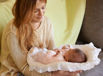 Νέα μαμά με νεογέννητο μωρό ξαπλωμένο σε στρωματάκι αγκαλιάς με λευκή θήκη