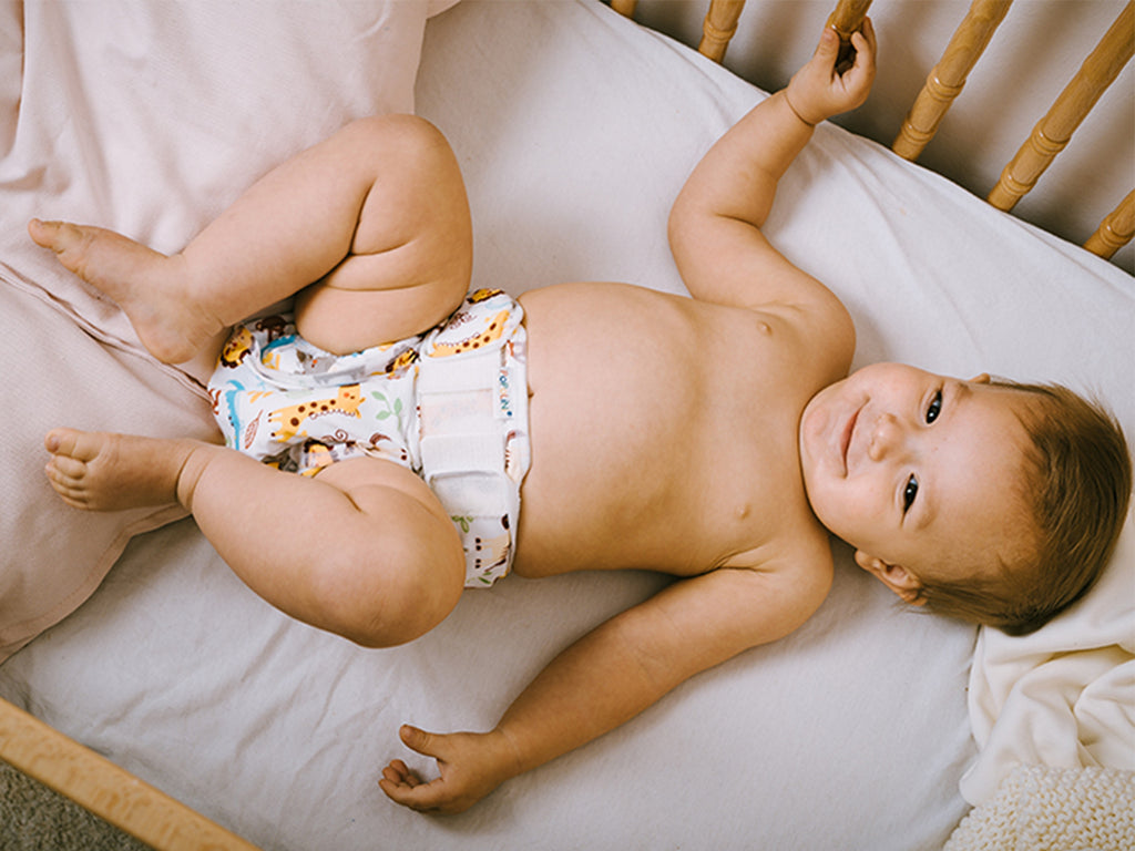 Μωρό ξαπλωμένο σε βρεφικό κρεβάτι φοράει υφασμάτινη πάνα Popolini και βρακάκι πάνας Popowrap.